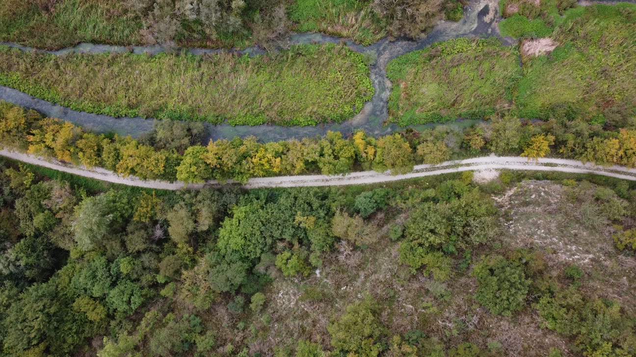 Flyfoto av en grusvei langs en bekk og et vegetasjonsbelte